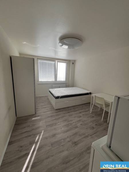 Garsonka s postelí, skříní, stolem a podlahou s dřevěným dekorem.