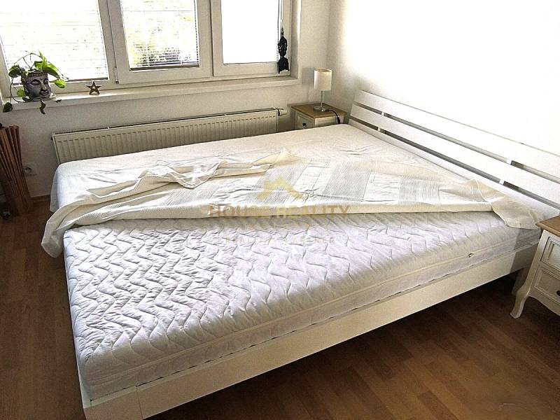 Světlá ložnice s bílou postelí a podlahou s dřevěným dekorem v 2-pokojovém bytě.