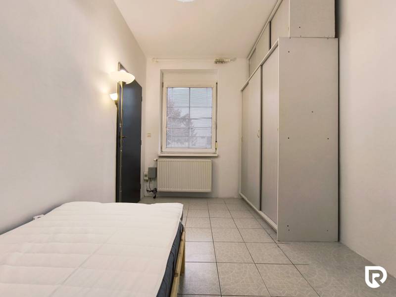 Pokoj v rodinném domě s postelí, šatníkem a oknem, podlaha s dlažbou.