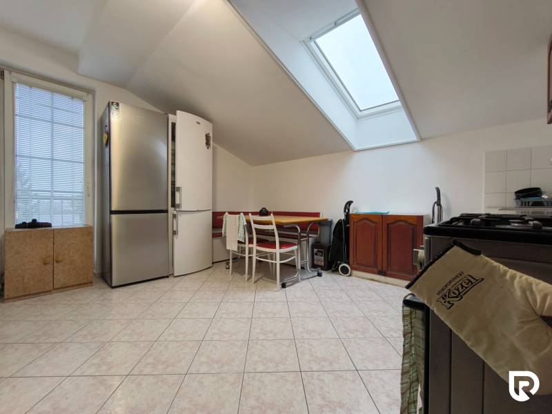 Kuchyně v rodinném domě se šikmým stropem, velkou lednicí a jídelním stolem.