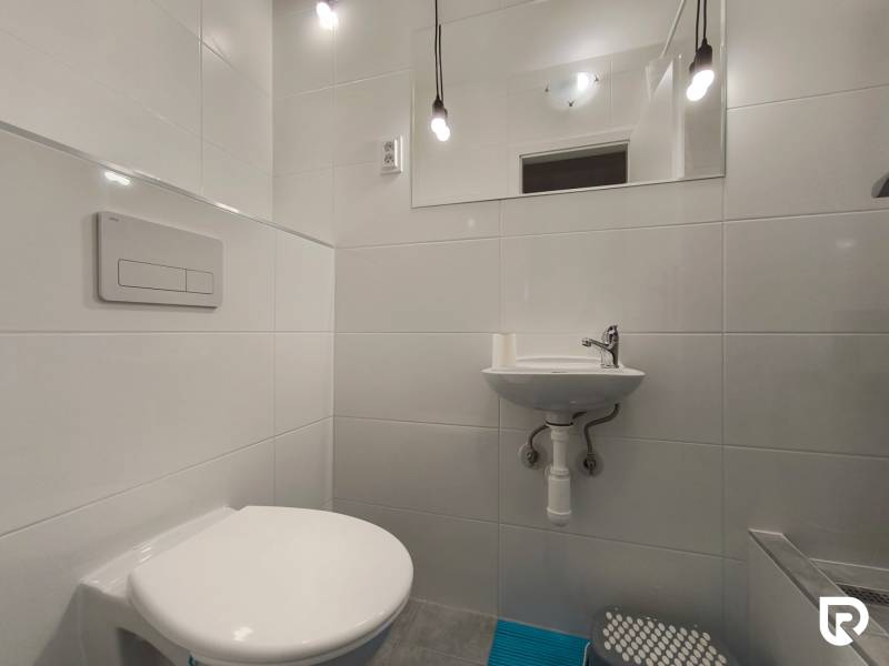 Koupelna v rodinném domě se závěsným WC, umyvadlem a svítidly.