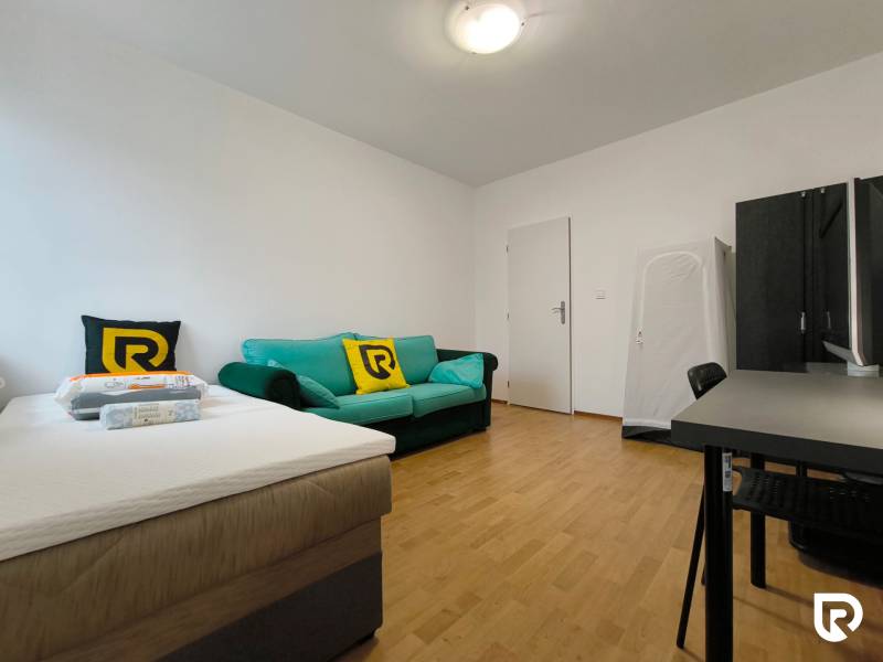 Pokoj v rodinném domě s postelí, pohovkou a pracovním stolem, podlaha s dřevěným dekorem.