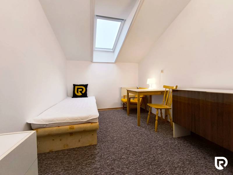 Jednoduchý pokoj s jednolůžkovou postelí, stolem a židlemi v rodinném domě.