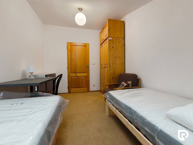 Pokoj v rodinném domě s postelemi, stolem, skříní a židlí.