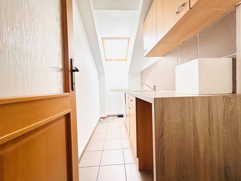 Úzká kuchyňská část v kanceláři s oknem a podlahou s dřevěným dekorem.