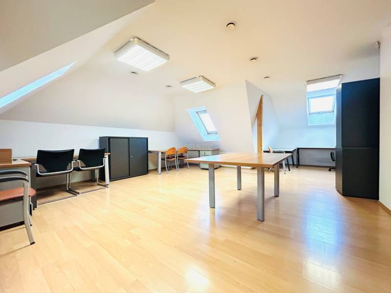 Podkrovní kanceláře s podlahou s dřevěným dekorem, střešními okny a kancelářským zařízením.