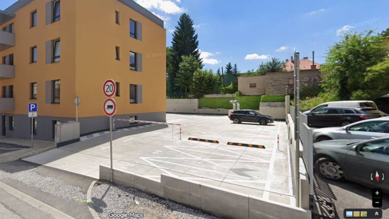 Parkoviště a obytná budova na Rudlovské cestě v Banské Bystrici obklopené zelení.