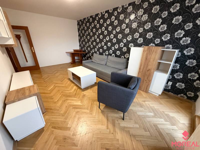 Obývací pokoj ve 3-pokojovém bytě s podlahou s dřevěným dekorem, vzorovanou tapetou a nábytkem.