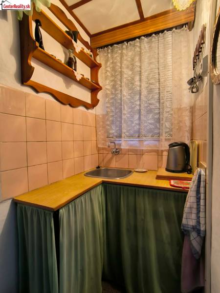 Kuchyňka v chatě s dřevěným dekorem, poličkou a závěsem u okna.