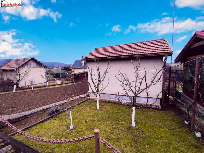 Zahrada s chatou v Partizánském, ovocné stromy a obdělávaná půda, jasná obloha.