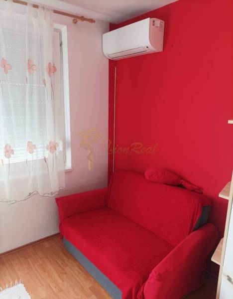 Červená pohovka, nástěnná klimatizace a záclona v 1-pokojovém bytě s podlahou s dřevěným dekorem.