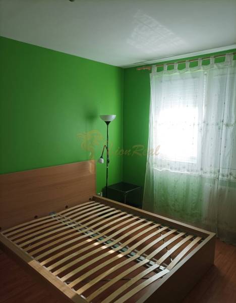 Ložnice v jednopokojovém bytě s postelí, zelenými stěnami a podlahou s dřevěným dekorem.