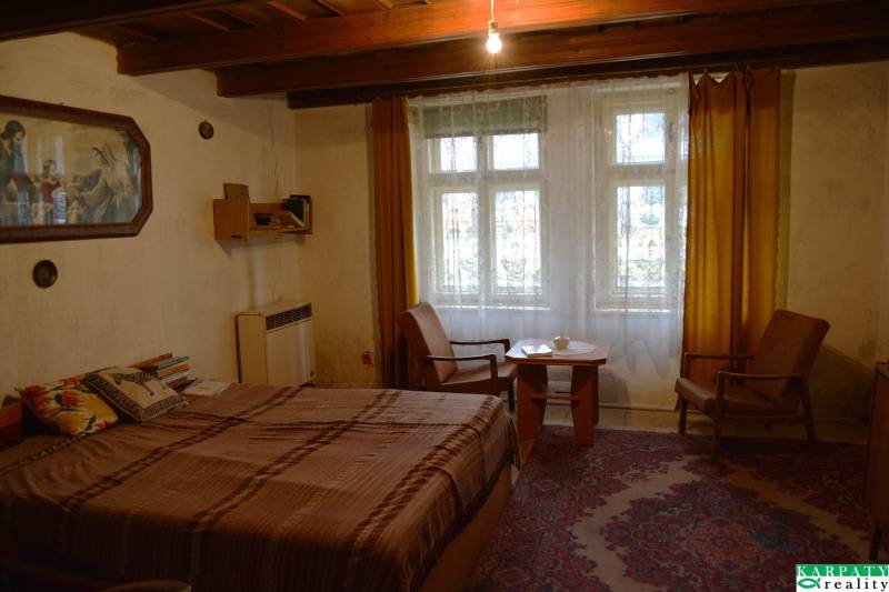 Pokoj v rodinném domě s postelí, křesly, žlutými závěsy a kobercem.