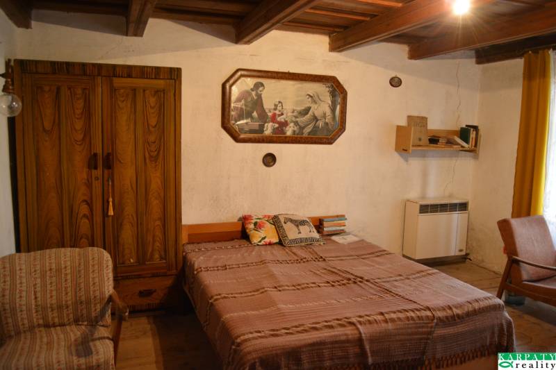 Ložnice v rodinném domě s dřevěnou skříní, postelí a obrazem na stěně.