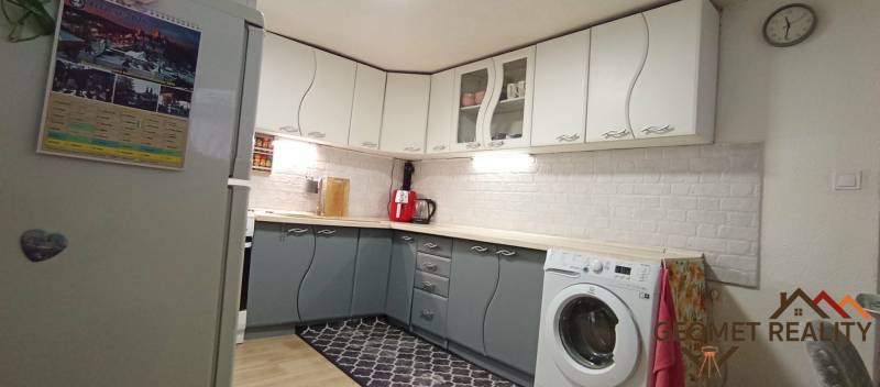 Kuchyně v rodinném domě s bílými a šedými skříňkami, podlaha s dřevěným dekorem.