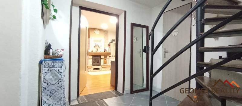 Interiér rodinného domu se schodištěm, podlahou s dřevěným dekorem a krbem.