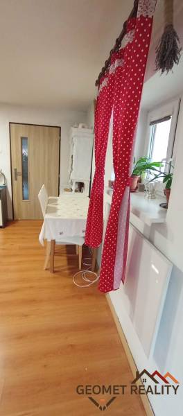 Jídelna v rodinném domě s červeným závěsem, stolem a podlahou s dřevěným dekorem.