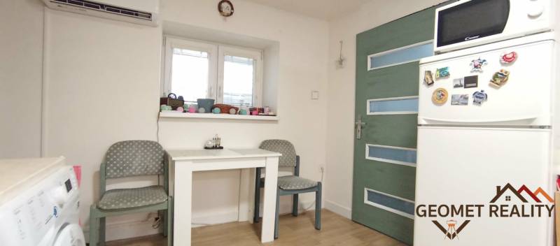 Jídelna v rodinném domě s bílým stolem, lednicí a podlahou s dřevěným dekorem.