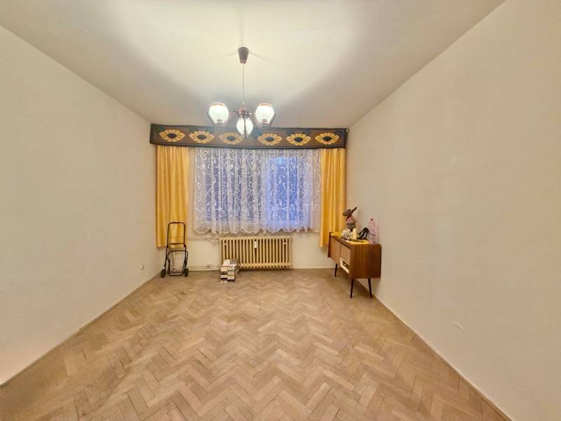 Pokoj v 3pokojovém bytě s podlahou s dřevěným dekorem, záclonami a komodou.