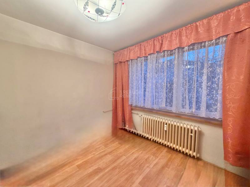 Pokoj v 3pokojovém bytě s podlahou s dřevěným dekorem a závěsy.