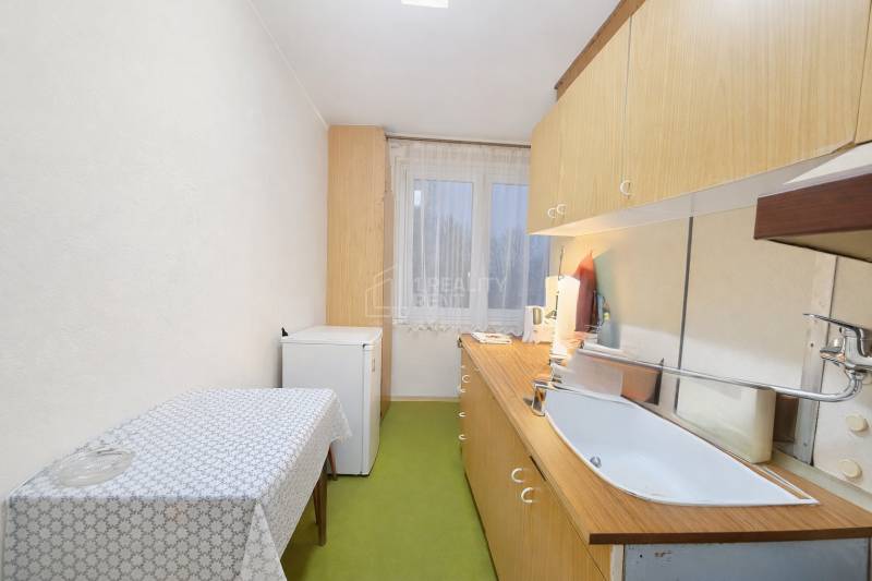 Kuchyně ve 3-pokojovém bytě s jednoduchým zařízením, podlaha s dřevěným dekorem.