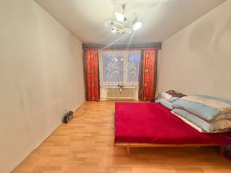 Ložnice v 3-pokojovém bytě s postelí, podlahou s dřevěným dekorem a světlem.