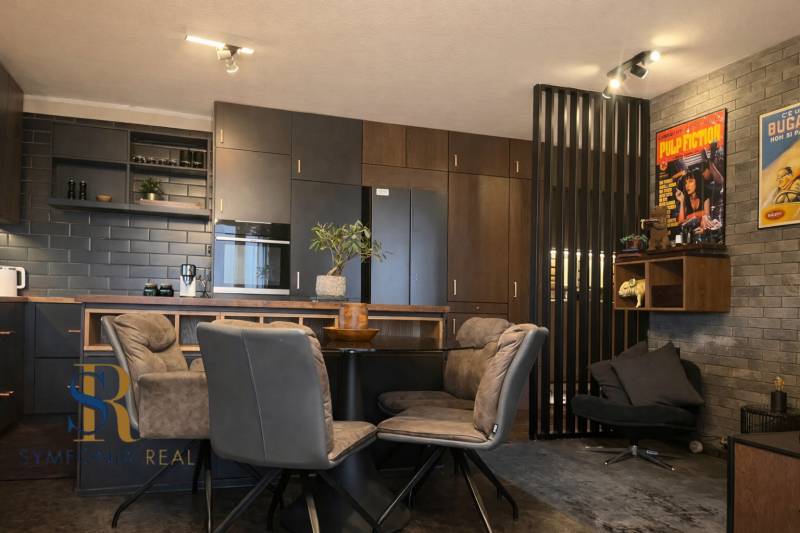 Kuchyně v 2-pokojovém bytě s tmavými skříňkami a dekorativními plakáty na stěně.