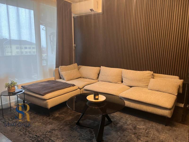 Světlá pohovka v 2-pokojovém bytě s dřevěným dekorem na stěně a stolkem.