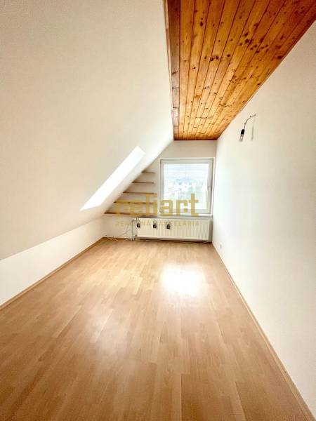Podkrovní pokoj v rodinném domě s podlahou s dřevěným dekorem a střešním oknem.