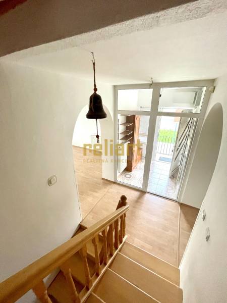 Schodiště s podlahou s dřevěným dekorem, vstupní dveře a zvonek v rodinném domě.