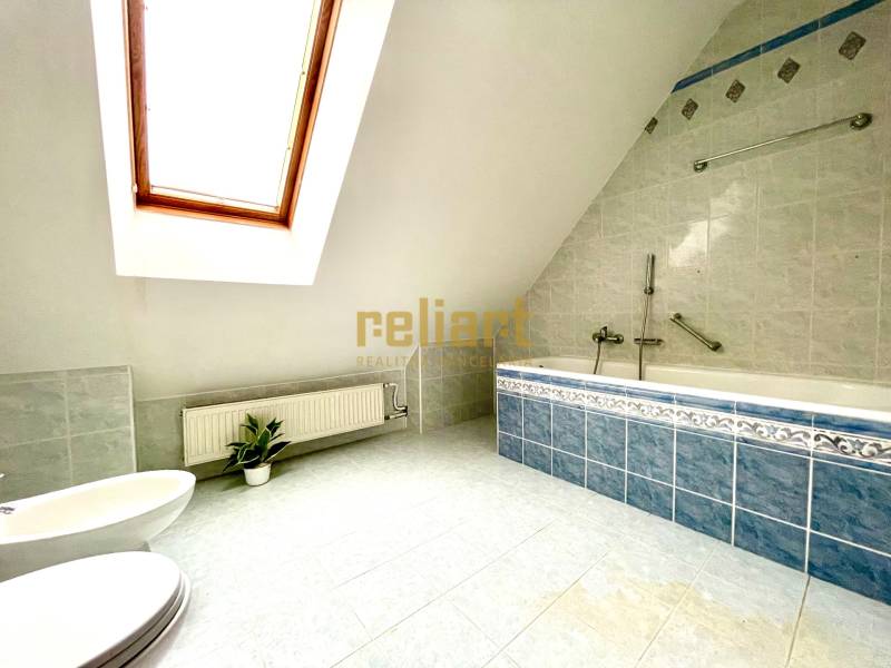 Podkrovní koupelna s rohovou vanou a střešním oknem v rodinném domě.