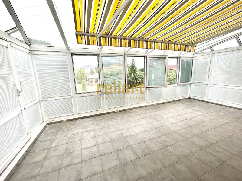 Zimní zahrada v rodinném domě s velkými okny a žlutými pruhovanými roletami.