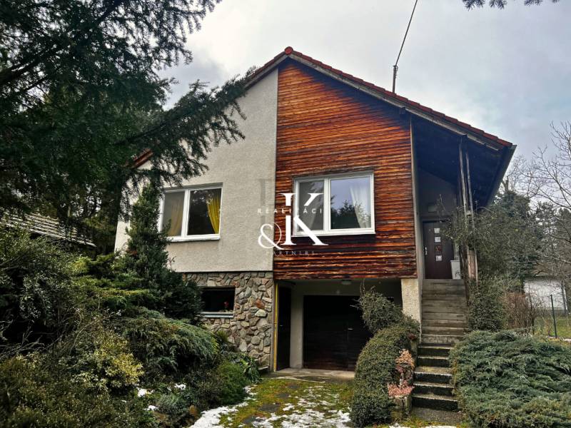 Chata v Modré s dřevěným obkladem a garáží, obklopená zelení.