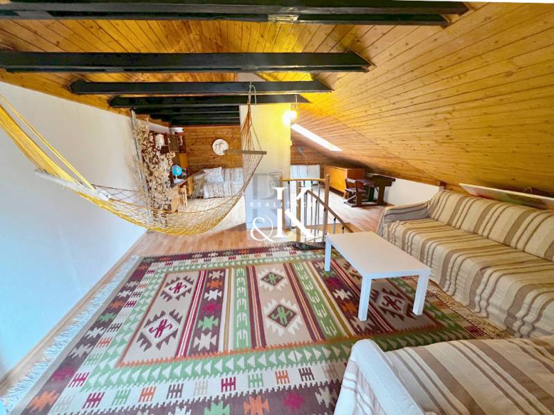 Podkroví chaty s pohovkou, houpací sítí a podlahou s dřevěným dekorem.