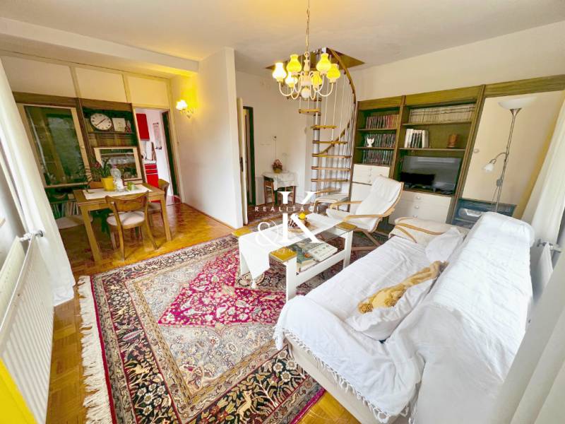 Interiér chaty se spirálovým schodištěm, televizí a stolem na podlaze s dřevěným dekorem.