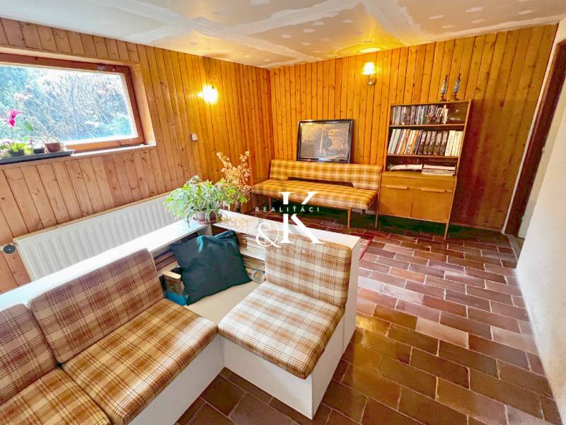 Interiér chaty s obývacím pokojem, rustikálním nábytkem a cihlovou podlahou.