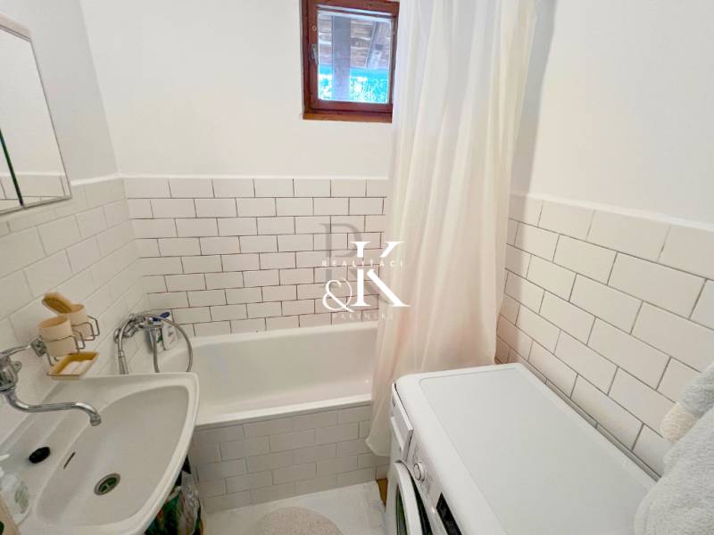 Koupelna v chatě s vanou, pračkou a bílým obkladem.