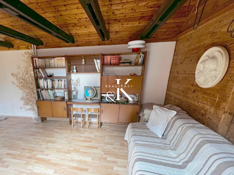 Interiér chaty s dřevěnými trámy, nábytkem a podlahou s dřevěným dekorem.