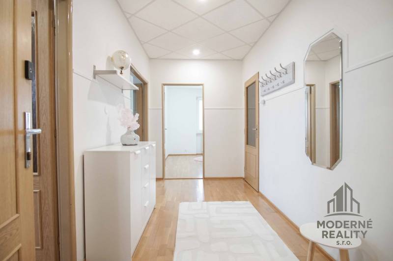 Chodba ve 4-pokojovém bytě s podlahou s dřevěným dekorem, jednoduše zařízená.