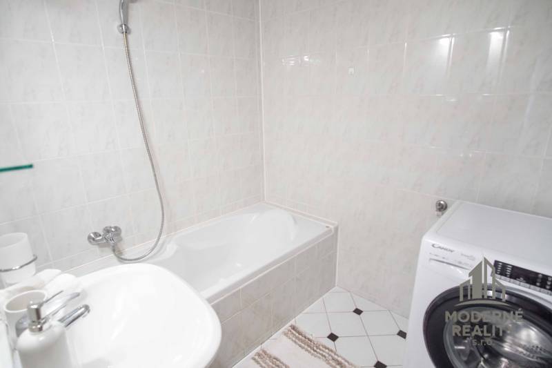 Koupelna se sprchovou vanou, umyvadlem a pračkou ve 4pokojovém bytě.