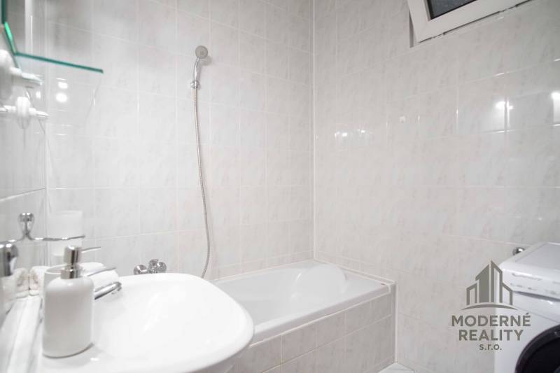 Koupelna s vanou a pračkou ve 4-pokojovém bytě. Stěny pokryté světlými obklady.