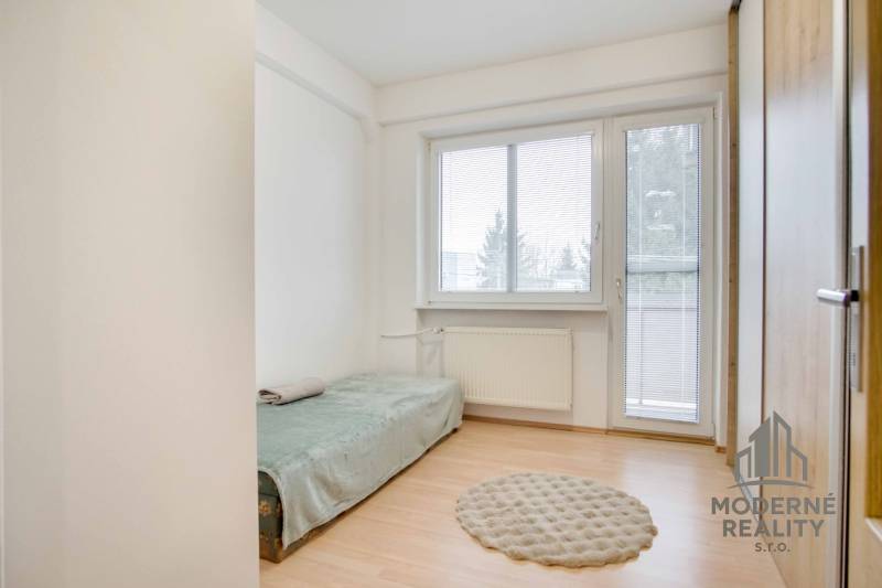 Jednoduchý pokoj s podlahou s dřevěným dekorem a rozkládací postelí ve 4pokojovém bytě.