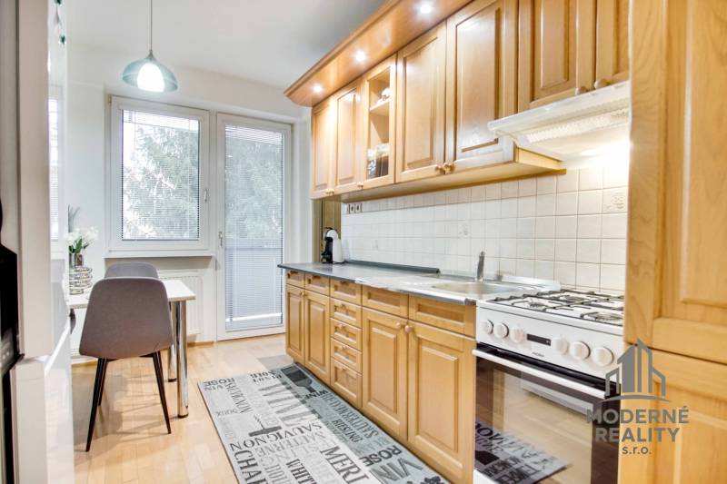 Kuchyně ve 4pokojovém bytě s podlahou s dřevěným dekorem a jídelním stolem.
