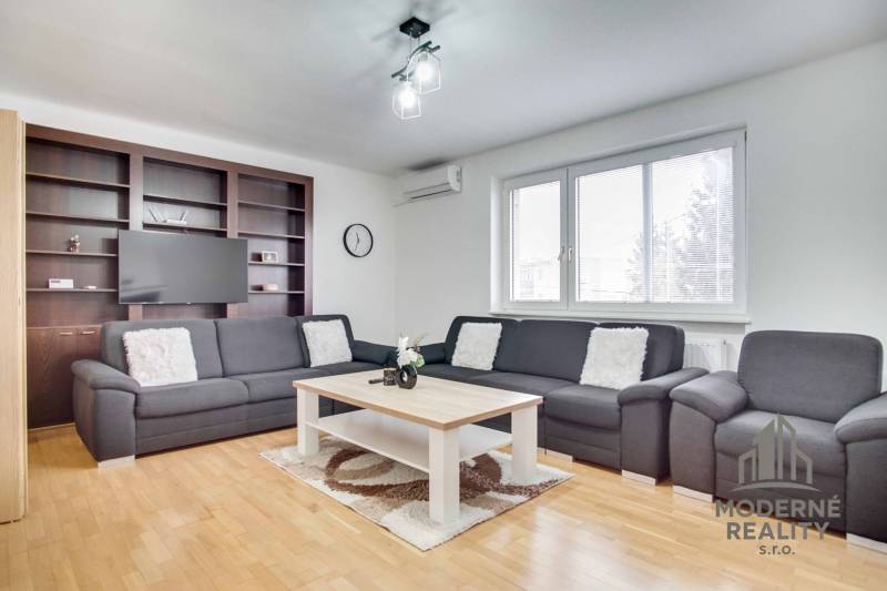 Obývací pokoj ve 4pokojovém bytě s pohovkou, konferenčním stolkem a podlahou s dřevěným dekorem.