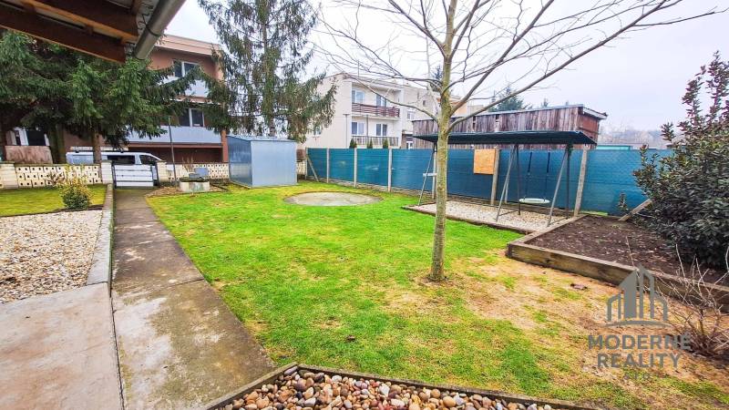 Zahrada u 4pokojového bytu v Kolte, se zelení, chodníkem a houpačkou.