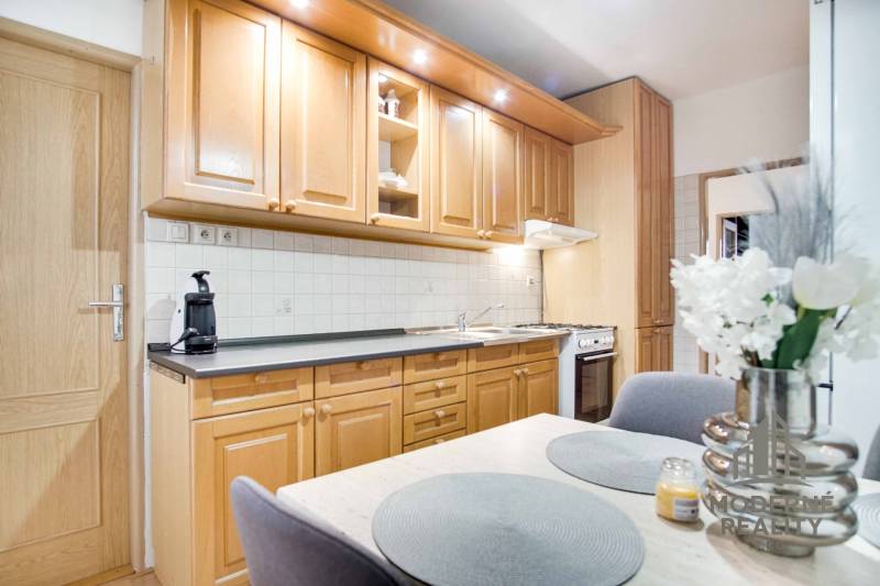 Kuchyně ve 4-pokojovém bytě s dřevěnými skříňkami, květinami a jídelním stolem.