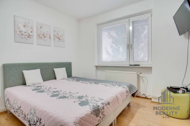 Ložnice ve 4pokojovém bytě s květinovými dekoracemi a televizí na stěně.