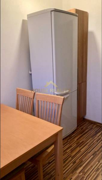 Kuchyně v 3-pokojovém bytě s lednicí, dřevěný stůl a židle, podlaha s dřevěným dekorem.