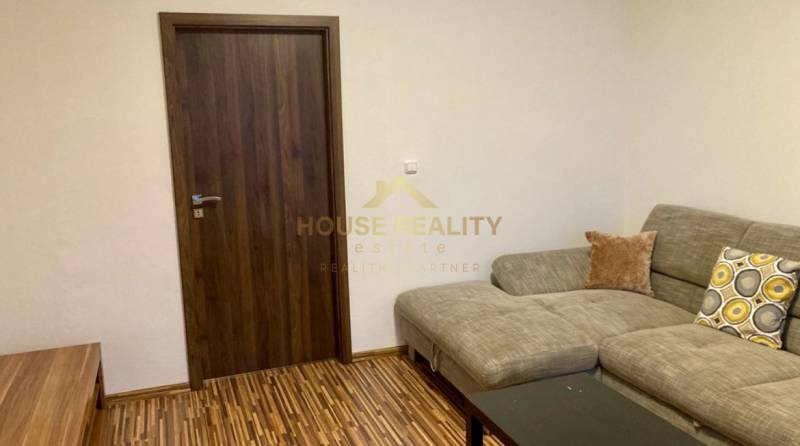 Obývací pokoj s pohovkou, dřevěná dekor podlaha a tmavé dveře ve 3-pokojovém bytě.