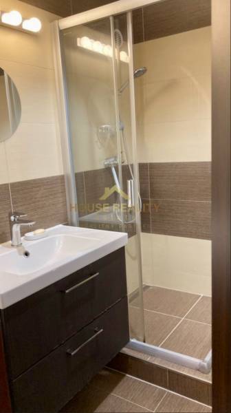 Koupelna s umyvadlem, sprchovým koutem a hnědými stěnovými obklady v 3-pokojovém bytě.